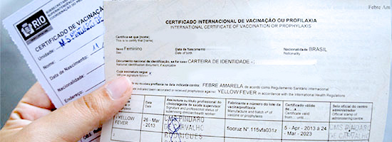 Mão segurando certificado internacional de vacinação e comprovante de vacinação da prefeitura do Rio de Janeiro